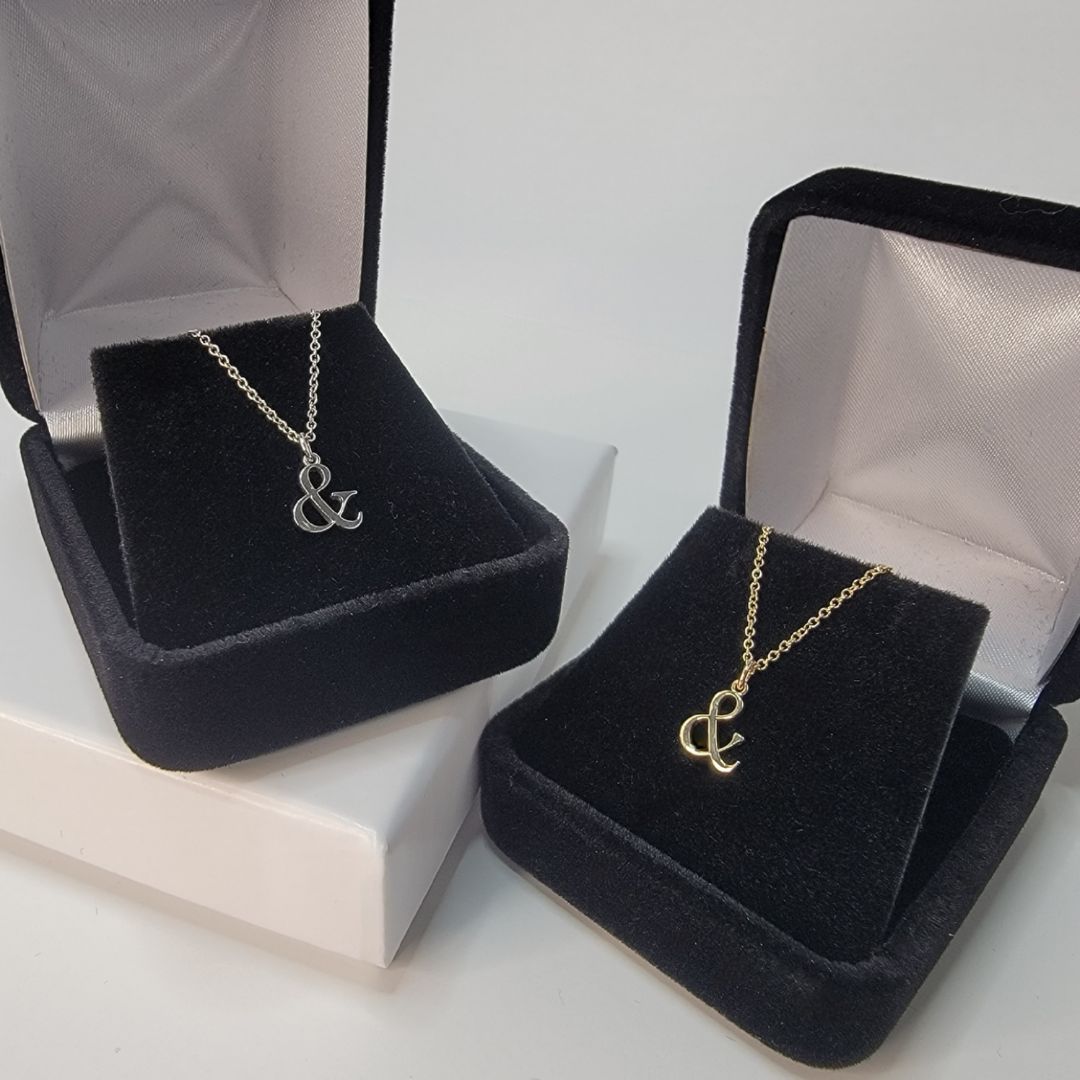 Two ampersand gold necklaces in display gift boxes one 14k white gold with diamond accents on the left and 14k yellow gold on the right  